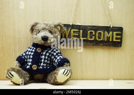 Begrüßungsschild und Teddybär auf Holzhintergrund Stockfoto