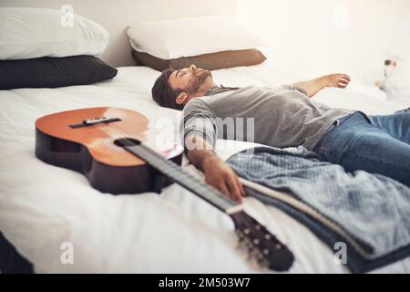 Ein kurzes Nickerchen, bevor ich wieder Spiele. Ein junger, gutaussehender Mann, der zu Hause neben seiner Gitarre schläft. Stockfoto