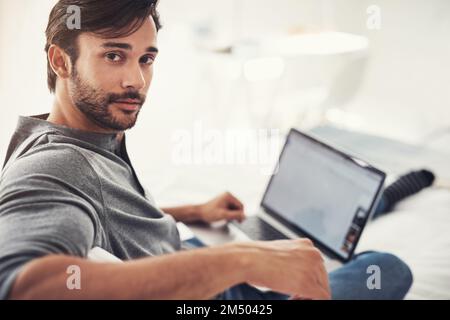 Er bekommt die beste Verbindung zu Hause. Ein gutaussehender junger Mann, der zu Hause im Netz surft. Stockfoto