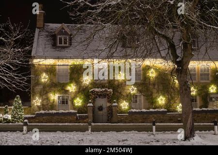 Weihnachtsdekorationen an der Vorderseite eines Hauses im Schnee bei Nacht. Broadway, Cotswolds, Worcestershire, England Stockfoto