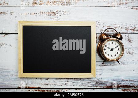 Wecker und Tafel auf Holzhintergrund Stockfoto
