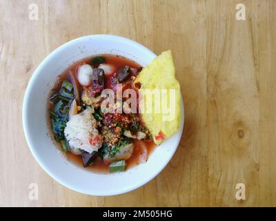 Yen ta fo oder Young tao fo. Eine thailändische Nudelsuppe mit Fischball, Tintenfisch, gebratenem Wanton und Gemüse in einer weißen Schüssel auf Holzhintergrund. Thailändisches Street Food Stockfoto