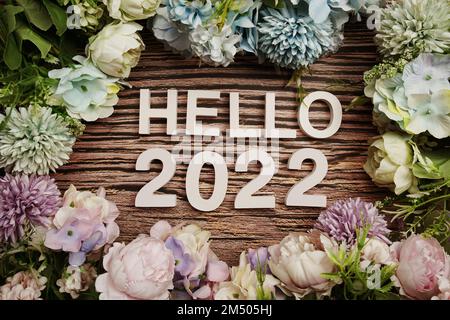 Hello 2022 Buchstaben schmücken mit Blumen auf Holzhintergrund Stockfoto