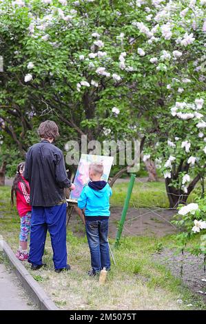 Kiew, Ukraine. 13. Mai 2013. Erwachsene Lehrer und Kinder, die im Freien auf einer Staffelei im Park Fliederblumen malten Stockfoto