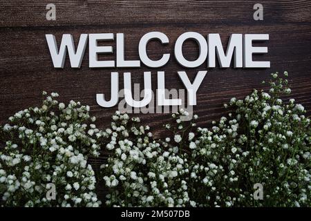 Begrüßungsbriefe im Juli mit Blumen auf Holzhintergrund Stockfoto