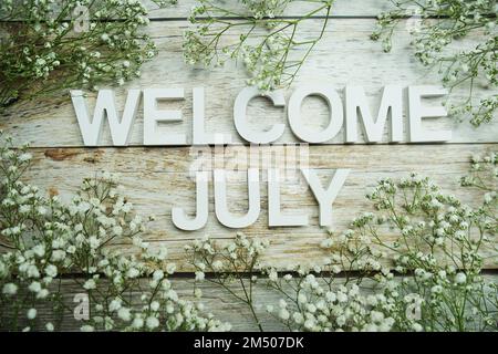 Begrüßungsbriefe im Juli mit Blumen auf Holzhintergrund Stockfoto