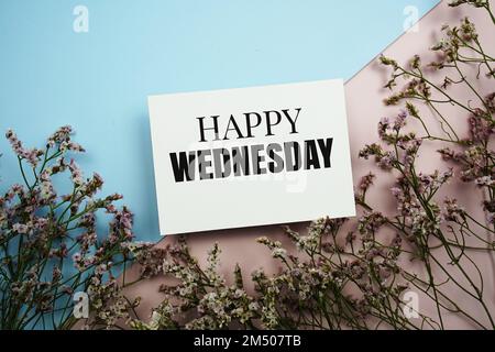 „Happy Wednesday“-Textnachricht mit Blume auf blauem und rosa Hintergrund Stockfoto