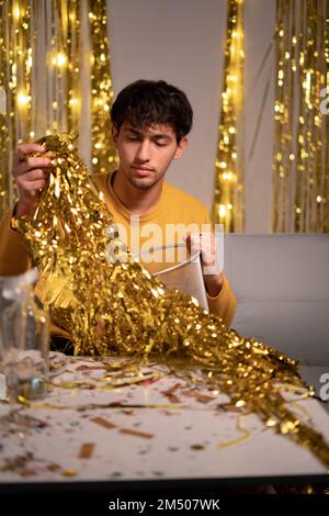 Ein Mann, der nach der Silvesterparty den Folienvorhang in den Mülleimer putzt. Speicherplatz kopieren Stockfoto