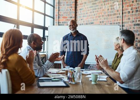 Was für eine tolle Art, ein Projekt zu starten. Eine Gruppe von Geschäftsleuten im Büro applaudiert einem Kollegen nach einer erfolgreichen Gruppenbesprechung. Stockfoto