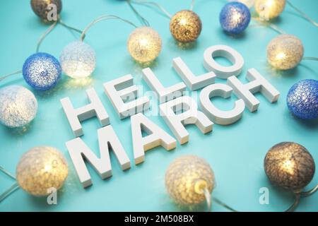 Der Buchstabe „Hello March“ dekoriert mit LED-Baumwollkugeln auf blauem Hintergrund Stockfoto