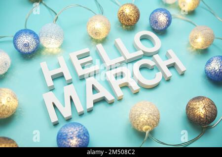 Der Buchstabe „Hello March“ dekoriert mit LED-Baumwollkugeln auf blauem Hintergrund Stockfoto