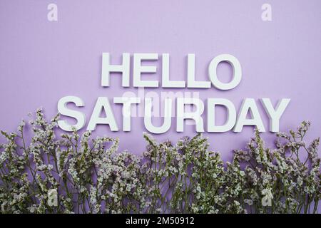 Hallo-Samstag-Buchstaben mit Blumenrahmen auf lila Hintergrund Stockfoto
