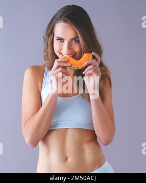 Nur ein Stück könnte dein Leben verändern. Studioaufnahme einer gesunden jungen Frau, die lächelt und posiert mit einer Scheibe Melone vor einem lila Hintergrund. Stockfoto