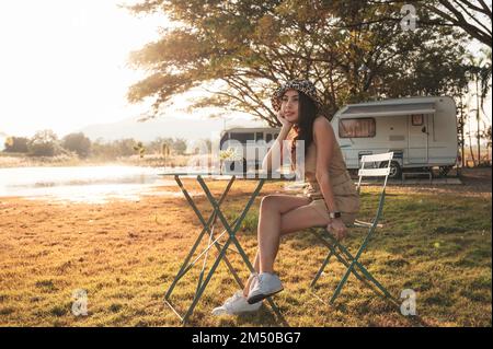 Wunderschöne junge asiatische Frau, die abends mit einem Wohnwagen am See auf dem Campingplatz parkte Stockfoto