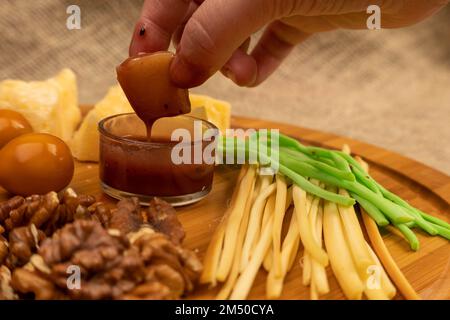 Jemand taucht ein Stück Käse in Honig vor dem Hintergrund verschiedener Käsesorten Stockfoto