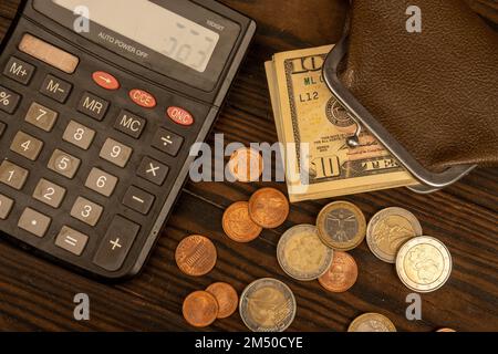 Dollar-Banknoten, Euro-Münzen, eine Vintage-Geldbörse aus braunem Leder und ein Taschenrechner auf einer Holzoberfläche. Nahaufnahme, selektiver Fokus. Stockfoto