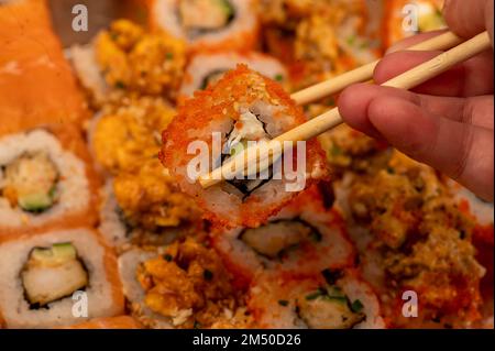 Jemand nimmt eine Essstäbchen Rolle aus einem Satz von verschiedenen Arten von Rollen in einer Box. Blick von oben auf verschiedene Portionen vegetarischer und Fischbrötchen. Nahaufnahme, Stockfoto