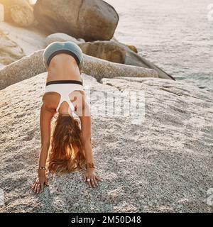 Finde dich selbst und sei so. Eine Frau, die am Strand die Hundehaltung mit dem Blick nach unten macht. Stockfoto