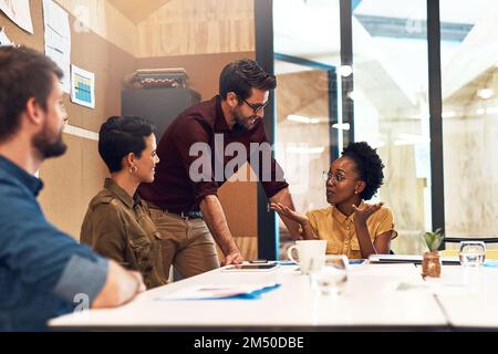 Sich ein paar innovative Ideen gegenseitig auszutauschen. Eine vielfältige Gruppe von Geschäftsleuten, die ein Meeting in einem Büro abhalten. Stockfoto