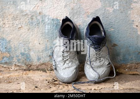 An der Wand stehen Sneaker, die stark mit grauer Farbe befleckt sind Stockfoto