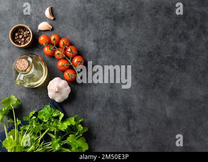 Gewürze und frische Kräuter Petersilie, Knoblauch, Pfeffer, Tomaten und Öl auf dunkelgrauem Hintergrund. Das Konzept der köstlichen und gesunden Küche. Draufsicht und Stockfoto