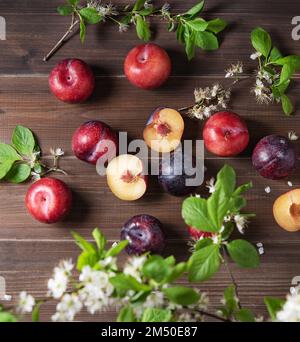 Ein paar saftige rote Pflaumen mit Blüten auf braunem Holzhintergrund. Bild in der Draufsicht Stockfoto