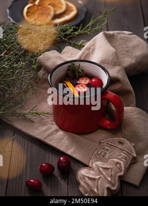 Köstlicher Weihnachtstee mit Orangen, Zimt, Cranbeeren und Gewürzen auf Holzhintergrund mit Lebkuchen, Orangen und Weihnachtsbaum. Stockfoto
