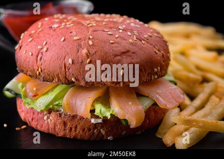 Roter Burger mit Lachs, Salat und Gurke, mit Kartoffeln und Sauce auf verschwommenem Hintergrund Stockfoto