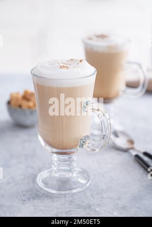 Zwei Gläser duftender Cappuccino-Kaffee mit Zimt auf einem blauen Tisch vor dem Hintergrund einer weißen Küche am frühen Morgen. Frühstück Konz Stockfoto