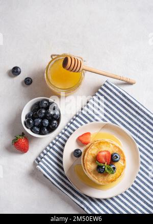 Hausgemachte klassische amerikanische Pfannkuchen im Stapel mit frischen Beeren und Honig auf einer gestreiften Serviette auf hellgrauem Hintergrund. Der Begriff der Heilung Stockfoto