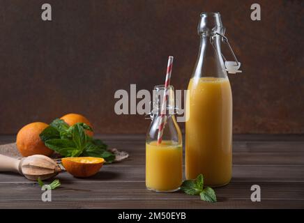 Frisch gepresster Orangensaft in zwei Flaschen mit Zitrusfrüchten auf braunem Holzhintergrund. Rustikales Konzept. Vorderansicht Stockfoto