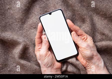 Telefon mit weißem Bildschirm in den Händen einer älteren Frau auf dem Tisch Nahaufnahme, weißer Bildschirm auf dem Telefon Stockfoto