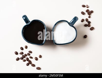 Zwei Tassen in Herzform mit frisch gebrühtem aromatischem Kaffee mit Milch und Espresso und verstreuten Körnern auf gelbem Hintergrund. Das Konzept des OP Stockfoto