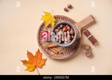 Herbstdecke mit bunten Ahornblättern mit Apfel und Nüssen auf Holzbrett auf orangefarbenem Hintergrund. Draufsicht und Kopierbereich. Stockfoto