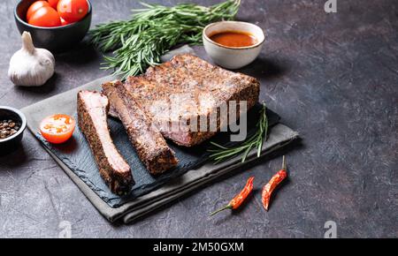 Saftige gegrillte Schweinerippchen mit Tomaten, Soße und frischen Kräutern auf dunklem Hintergrund. Picknick-Produktkonzept. Speicherplatz kopieren. Stockfoto