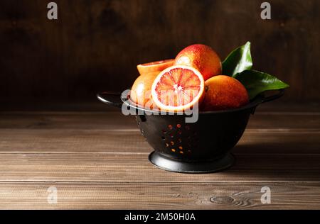 Saftige sizilianische rote Orangen in einer schwarzen Schüssel auf dunklem Holzhintergrund. Vorderansicht und Kopierbereich. Stockfoto