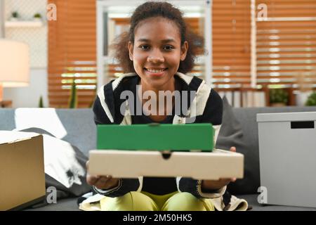 Glückliche junge Frau, die Essensbehälter zum Mitnehmen, Pizzakarton und ein Lächeln vor die Kamera hielt Stockfoto