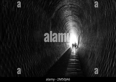 Eine Graustufenaufnahme von zwei Personen, die im Fußgängertunnel in den Chotkovy-Gärten in Prag, Tschechisch, spazieren gehen Stockfoto