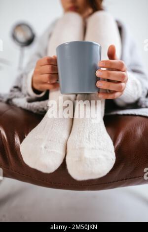 Nahaufnahme Foto süße Frau entspannend mit heißem Getränk überzogene Decke trägt Haushaltskleidung Kleidung Outfit Sitz bequemer Sessel Stockfoto