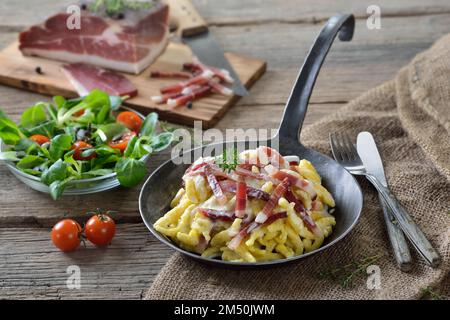 Herzhafter Spaetzle mit Käsesauce und Südtiroler Speck, serviert in einer eisernen Bratpfanne Stockfoto