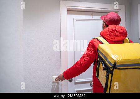 Ein Liefermann an einer Haustür läutet die Glocke. Lieferkonzept für Speisen und Getränke. Stockfoto
