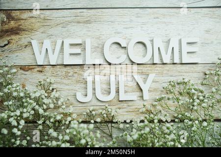 Begrüßungsbriefe im Juli mit Blumen auf Holzhintergrund Stockfoto