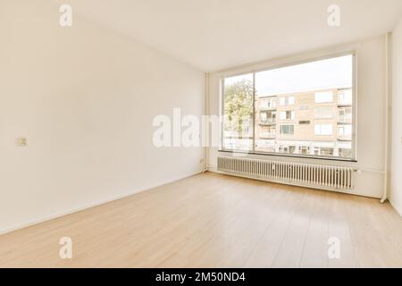 Ein leerer Raum mit weißen Wänden und Hartholzböden, es gibt ein großes Fenster im Zimmer ohne Fenster Stockfoto