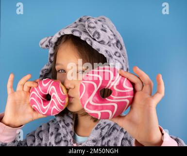 Mädchen in Kigurumi oder Pyjama mit Donuts anstelle der Augen auf blauem Hintergrund. Hochwertiges Foto Stockfoto