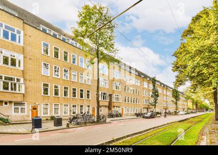 Die Straße vor einem Apartmenthaus mit Fahrrädern, die auf dem Gehweg geparkt sind und Bäume, die die Straße säumen Stockfoto