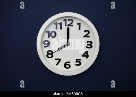 Weiße Uhr mit acht Uhr auf blauem Hintergrund Stockfoto