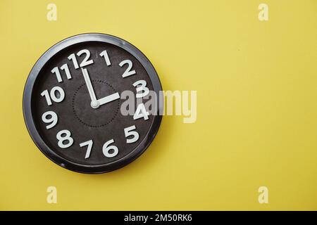 Schwarze rund-Uhr-Anzeige mit 11 Uhr auf gelbem Hintergrund Stockfoto