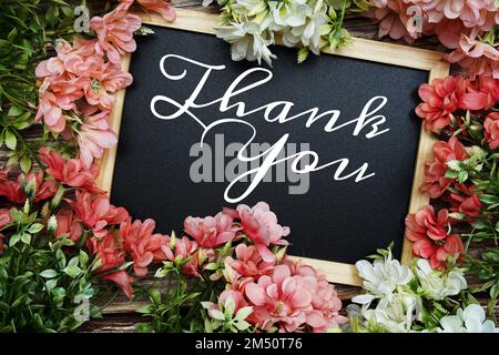 Dankeschön-Schriftzug auf Holztafel mit Blumenstrauß auf Holzhintergrund Stockfoto