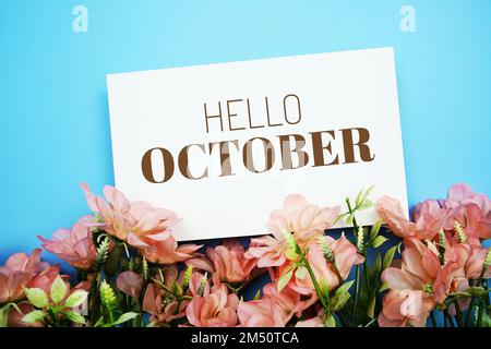 „Hello October“-Textnachricht mit Blumendekoration auf blauem Hintergrund Stockfoto