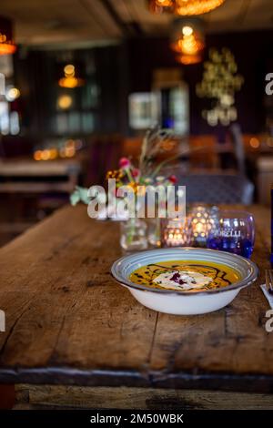 Ein vertikaler Schuss Kürbissuppe, serviert in einer Schüssel auf einem Holztisch in einem Café Stockfoto